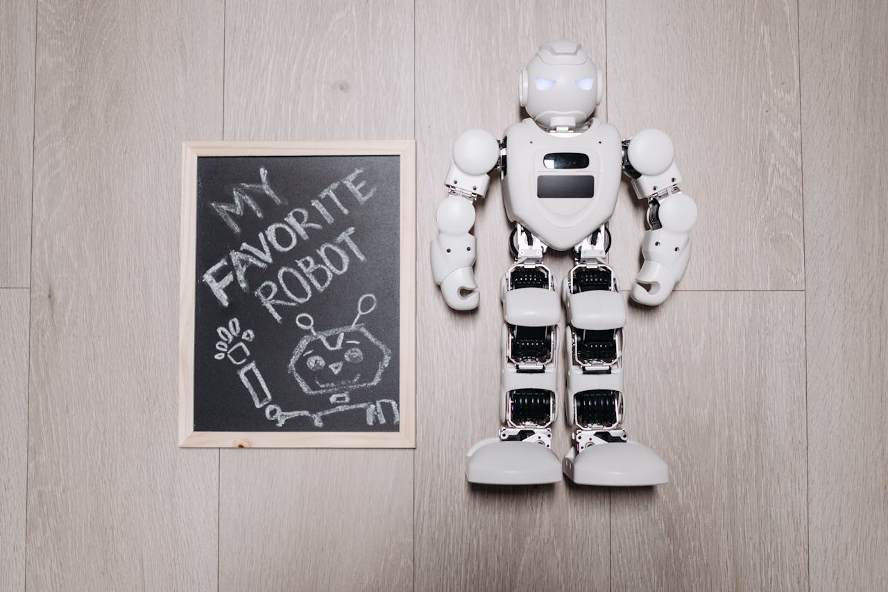 Overhead shot of a robot toy alongside a chalkboard drawing, on a light wooden floor.